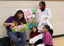  Woman in purple reads to two girls sitting and one girl standing